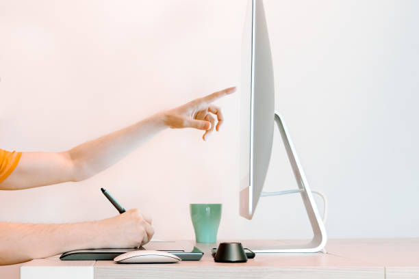 istock Graphic designer points screen, wears orange shirt 1227201546