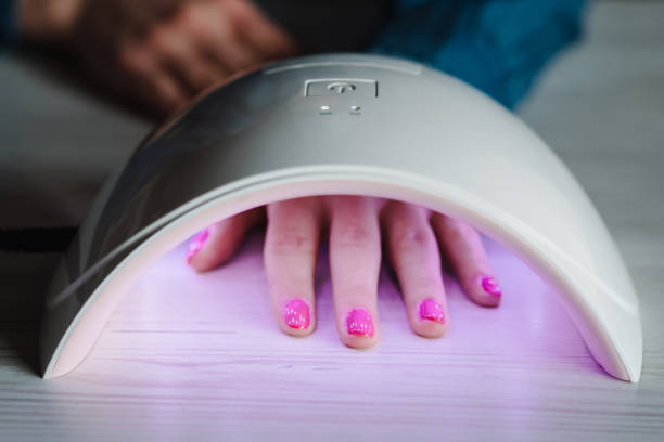 istock Woman hand inside lamp for nails on table close up. UV lamp with light for drying nails with gel polish. violet nails dried in the lamp. Girl makes a manicure at home, doing manicure herself, draws. 1227205837