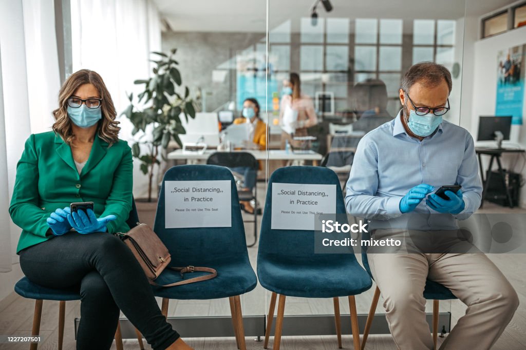 Concept of social distancing to prevent spread of infectious disease Customers using mobile phone wearing protective masks and gloves sitting on office chair while maintaining social distance to protect from COVID-19 Bank - Financial Building Stock Photo