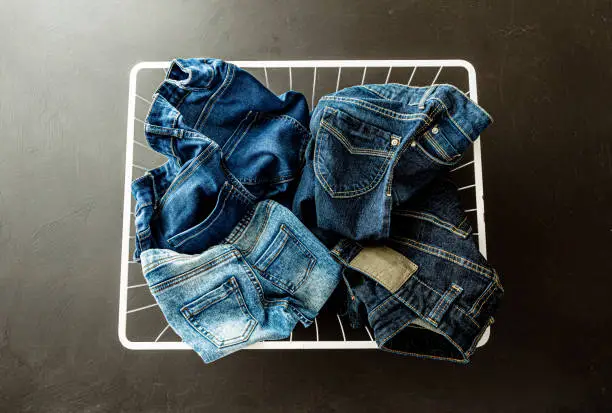 Photo of Family jeans in laundry (washing) basket on black - denim trousers