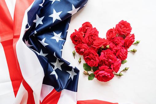 Independence Day USA concept. Memorial Day. Heart shape of red roses with the US flag flat lay top view