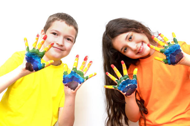 少年と10歳の少女がカメラを見て、手のひらをペンキで見せます。手に虹。幸せな子供時代と子供の日の概念。テキスト用のスペース - 12 13 years ストックフォトと画像