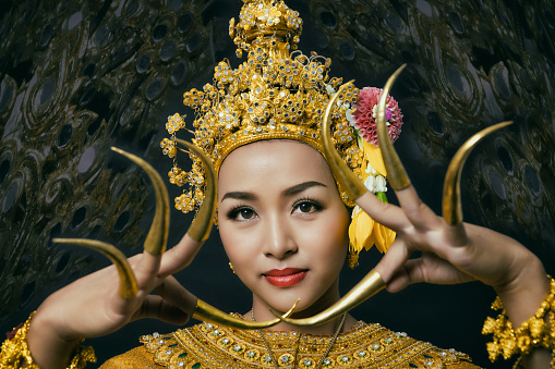Beautiful Thai woman wearing traditional golden dancer dress with headgear jewelry long nails looking smiling to camera on background.