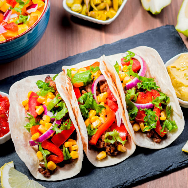 istock Table with tacos, mango salsa, nachos with sauce, guacamole, lemon beer. Appetizers and traditional mexican dishes for cinco de mayo or taco tuesday on wooden table top, copy space 1227211381