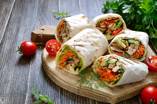 Fresh tortilla wraps with chicken, mushrooms and fresh vegetables on wooden board. Chicken Mexican burrito. Tasty appetizer. Dishes from pita bread. Healthy food concept.