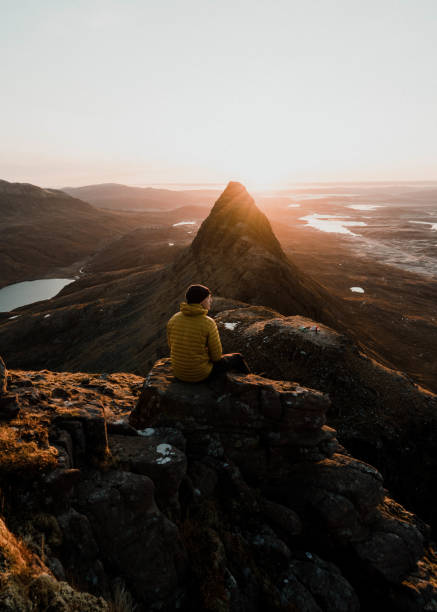 istock Man sits on grassy knoll; mountains in distance 1227221938
