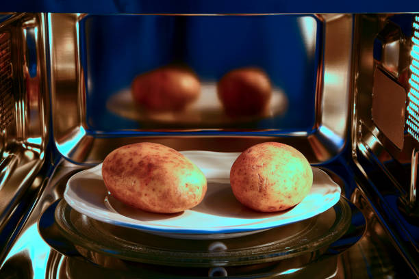 dos patatas al horno listas para cocinar en un horno microondas - patata al horno fotografías e imágenes de stock