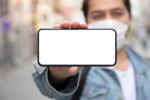 istock Young man stretches his smart phone to the camera while wearing a protective mask 1227225020