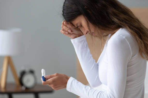 Unhappy stressed woman crying, feeling depressed, holding pregnancy test Unhappy stressed woman crying, feeling depressed, holding pregnancy test in hand close up, sitting in bedroom at home, dissatisfied by result, unwanted pregnancy or health problem, infertility unwanted pregnancy stock pictures, royalty-free photos & images