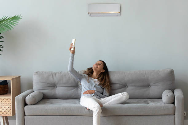 istock Smiling woman relaxing on couch, using air conditioner remote controller 1227225927