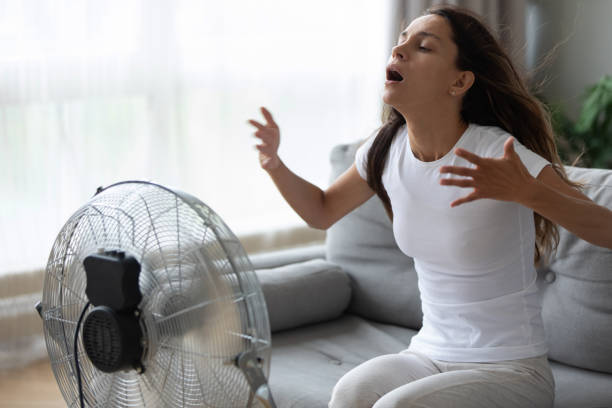Overheated woman enjoying fresh air, cooling herself by electric fan Overheated woman enjoying fresh air, cooling herself by electric fan close up, exhausted tired pretty girl sitting on couch in front of ventilator, suffering from hot summer weather at home overheated photos stock pictures, royalty-free photos & images