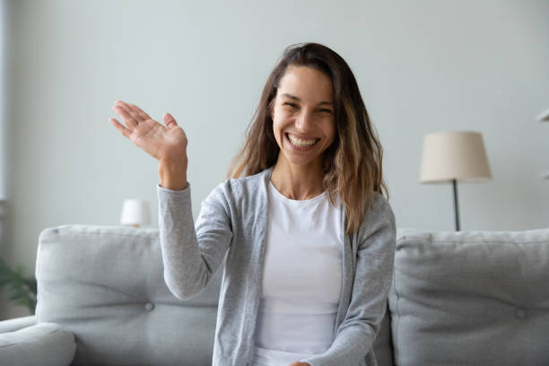 Happy young woman waving hand, looking at camera