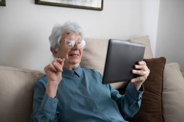 feliz mujer mayor haciendo videollamada en una tableta en casa - portrait senior adult confusion women fotografías e imágenes de stock