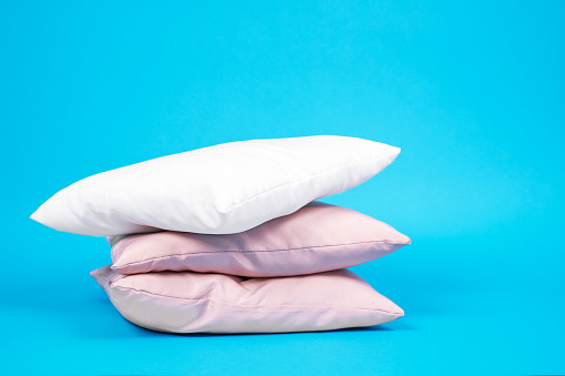 Three pillows stacked on top of each other, white and pink color, on bright blue background. Bed linen and bedding, housekeeping. Indoors, copy space.