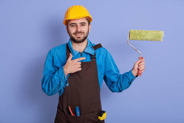 istock Image of energetic charismatic good looking young manual worker smiling sincerely, being at work, making gesture, holding roller in one hand, showing direction with forefinger. Profession concept. 1227228812