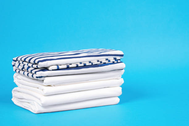 istock Striped and snowy white bed linen, neatly folded sheets on blue background. The concept of cleanness and proper storage organization. Indoors, copy space. 1227228823