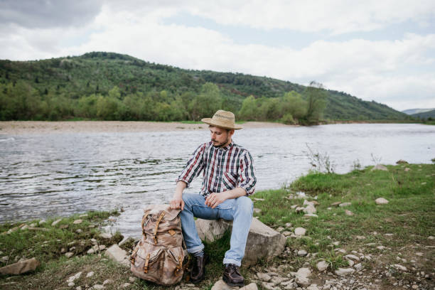 istock A young man with a backpack sitting on a rock by the mountain river 1227229551