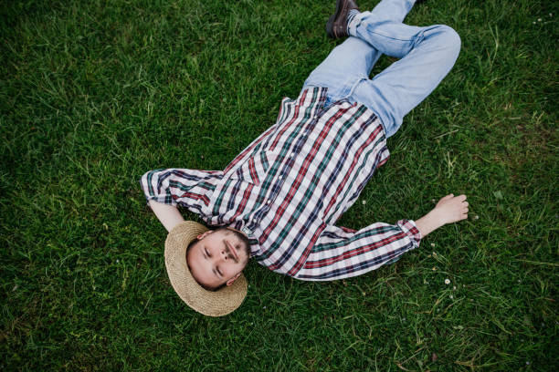 istock Young man farmer in a straw hat lying on the green grass, top view 1227229620