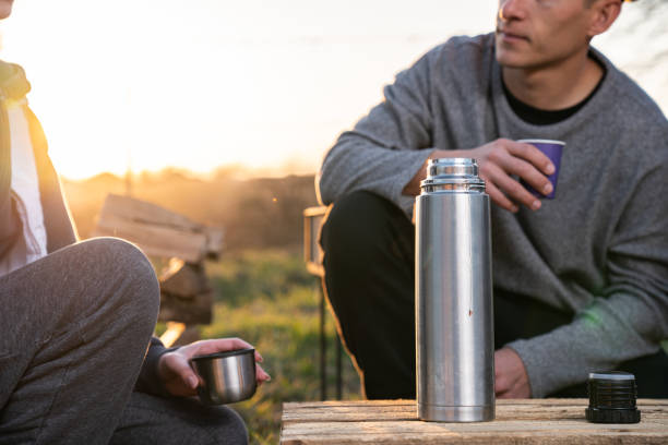 istock Wearing casual clothes man in drinking hot tea from a metal thermos while spending lunch break with girlfriend, sun lights on the background 1227233451