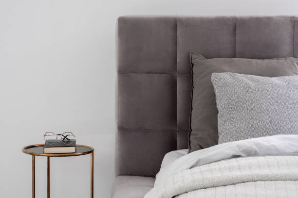 Bed with round bedside table Close-up on gray quilted bed with round, golden bedside table in white wall bedroom bed decoration stock pictures, royalty-free photos & images