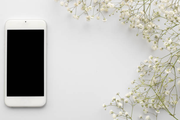 istock Top view cellphone with blank screen with flowers on white background. Flat lay floral frame with copy space. 1227235735