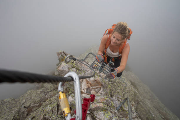 pov past carabiner to woman climbing up a via ferrata in the mist - leadership risk cliff mountain climbing imagens e fotografias de stock