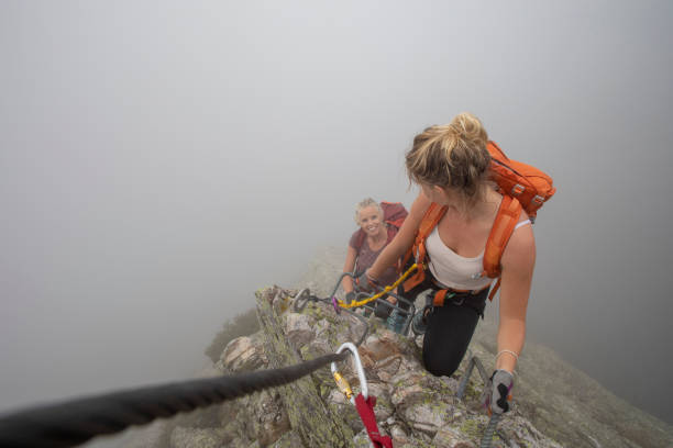 pov past carabiner to young woman climbing up a via ferrata in the mist - leadership risk cliff mountain climbing imagens e fotografias de stock