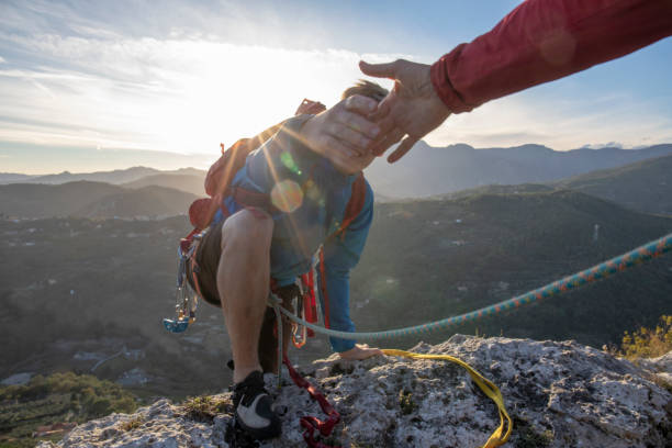 bras vers le bas de pov au jeune homme grimpant vers le haut d’une face rocheuse - climbing mountain climbing rock climbing moving up photos et images de collection