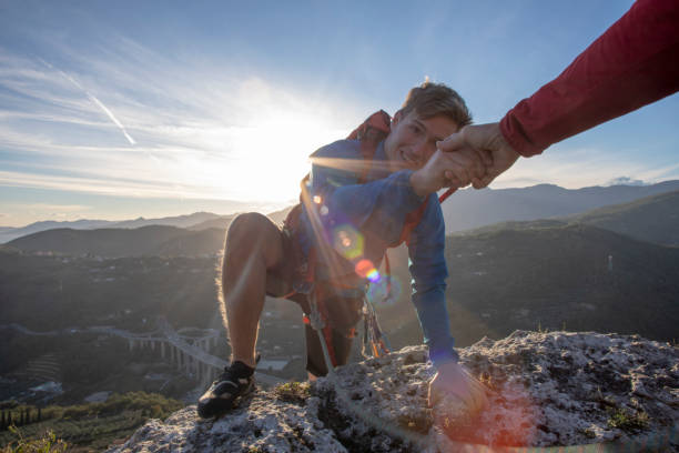 POV down arm to young man climbing up a rock face The sun is rising over the distant hills clambering photos stock pictures, royalty-free photos & images