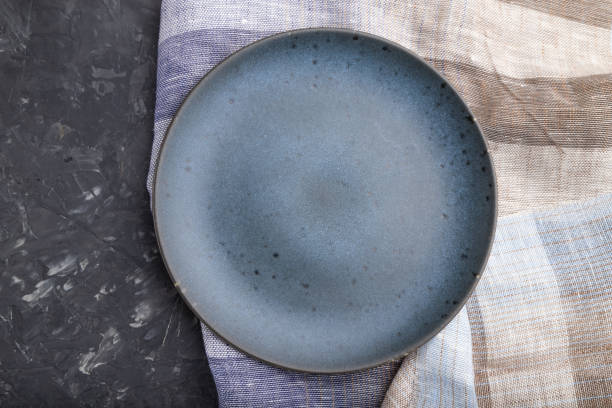 istock Empty blue ceramic plate on black concrete background and linen textile. Top view, flat lay, close up. 1227243542