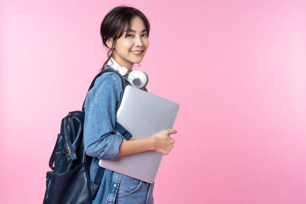 verticale du jeune étudiant asiatique de sourire avec l’ordinateur portatif et le sac à dos isolés au-dessus du fond rose - mannequin métier photos et images de collection