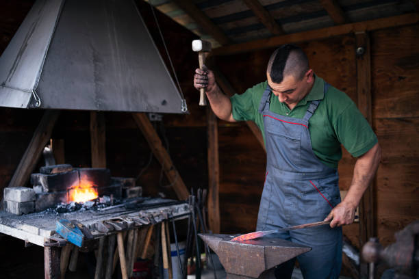 Shot of two blacksmiths in their workshop in Malaysia. They are  working with metal. Focus on anvil and hammer in front.