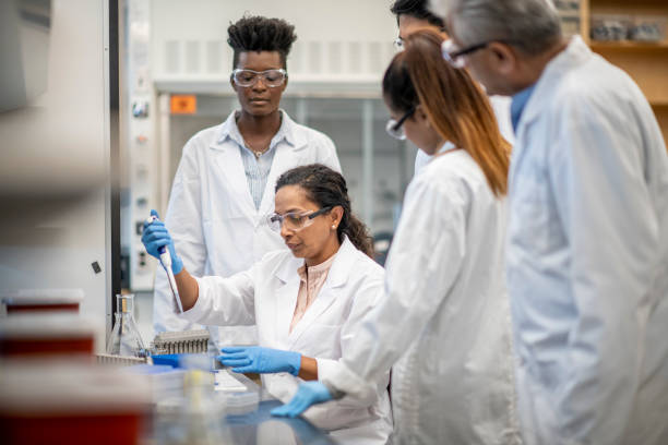 istock Female chemistry professor using a pipette in the lab with students observing her actions 1227267600