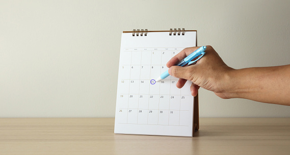 Hand with pen mark at 15th on calendar date
