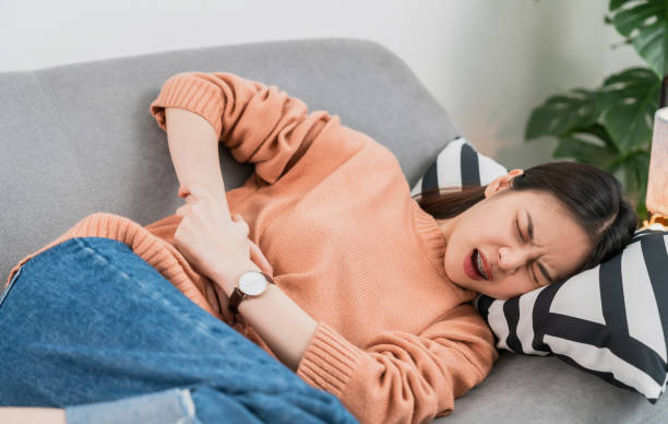 Young Asian woman hands holding the stomach on sofa and pain period cramps because having menstruation. Young Asian woman hands holding the stomach on sofa and pain period cramps because having menstruation. pms photos stock pictures, royalty-free photos & images