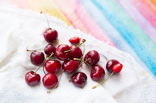 ripe juicy red cherries in drops of clear water on white cotton napkin on bright multi-colored wooden cover