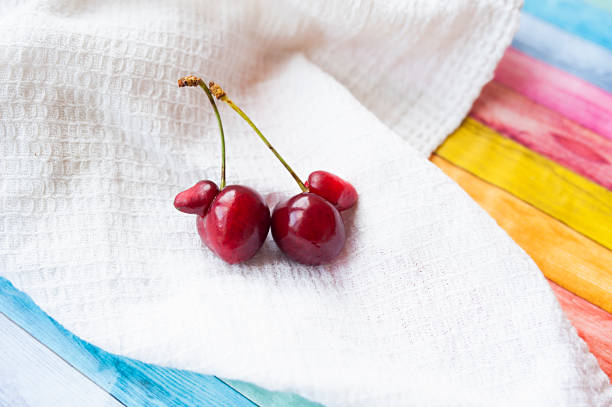ripe ugly strange red cherries in drops of clear water on white cotton napkin on bright multi-colored wooden cover