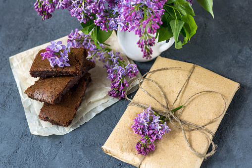 Spring composition with gift box, lilac flowers and brownie, wet cake. Dessert for served for tea or coffee break. Snack on a spring day in the garden.