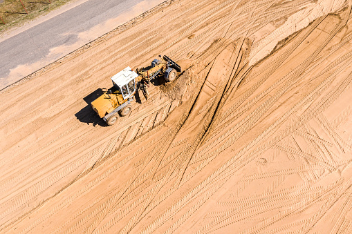 road construction site with heavy machinery. yellow grader levels the ground for construction. aerial view