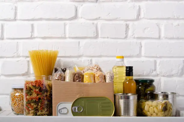 Set of uncooked foods on pantry shelf prepared for disaster emergency conditions on brick wall background