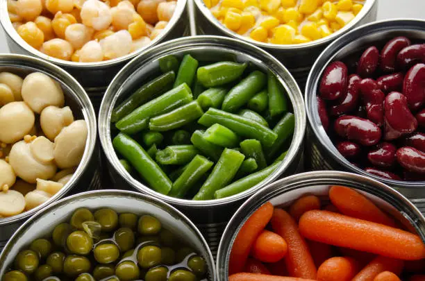 Photo of Canned vegetables in opened tin cans on kitchen table. Non-perishable long shelf life foods background