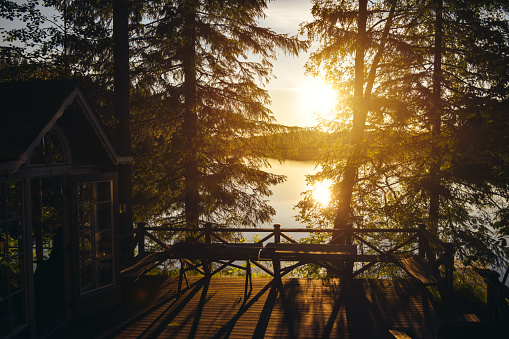 Sunset lake view from a typical summer cottage with sauna in Finland with big pine trees and wooden floor with barbecue zone