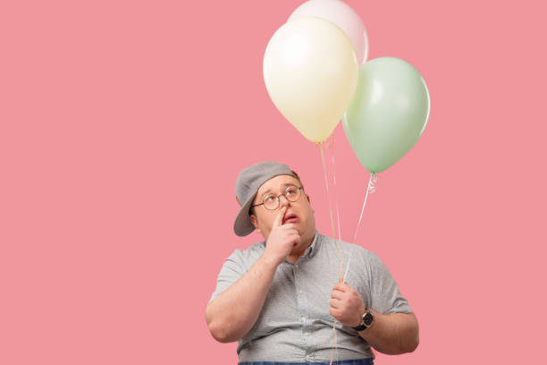istock Funny plump guy standing with air balloons having doubts isoated on pink 1227295210