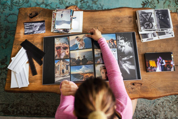 Young Adult woman adding photos to a photo album at home Young Adult woman adding photos to a photo album at home photo album photos stock pictures, royalty-free photos & images