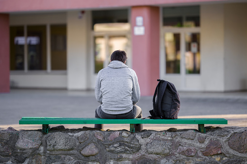 Un joven sentado en el banco del patio de la escuela. Tiempo de descanso. Vista trasera. photo