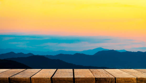 istock Empty display wooden board shelf counter with copy space for advertising backdrop and background with orange teal sunset silhouette mountain. 1227305972