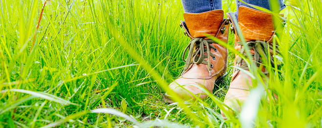 Female legs shod in Hiking boots on the green grass. Travel concept