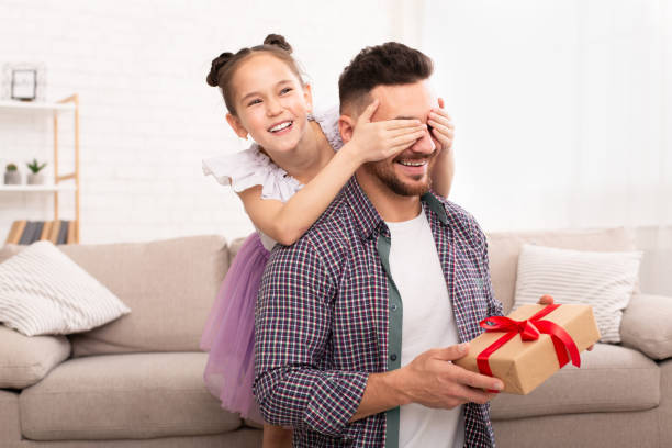 istock Playful daughter surprising her dad, closing his eyes and giving gift 1227310865