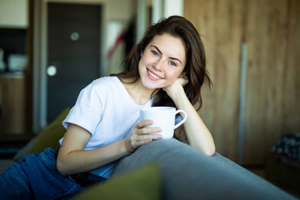 istock Young woman sitting sideways on the couch, while looking forward and smiling with a mug in her hands. 1227310938
