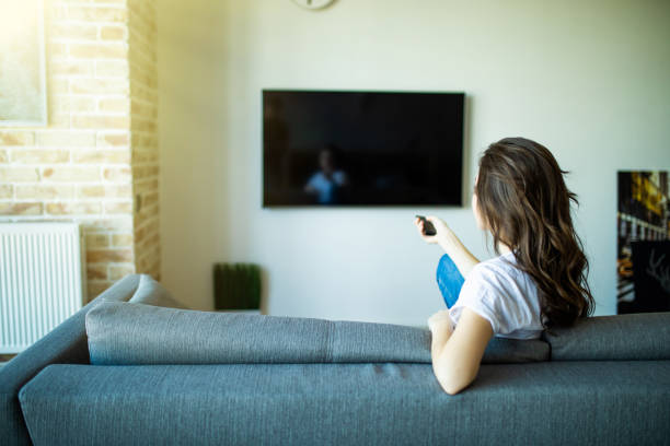istock Young woman changing channels with remote control on tv 1227310967